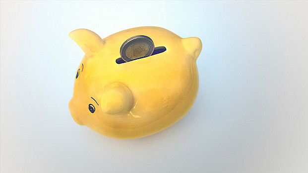 Ein gelbes Sparschwein mit einem Euro im Einwurfschlitz